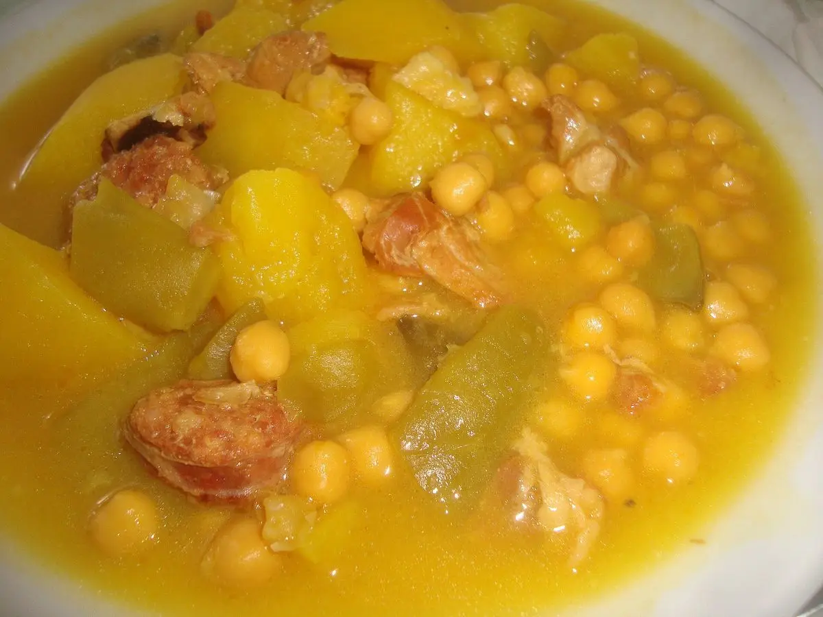 Plato hondo de garbanzos guisados con trozos de patata, carne y chorizo en caldo dorado