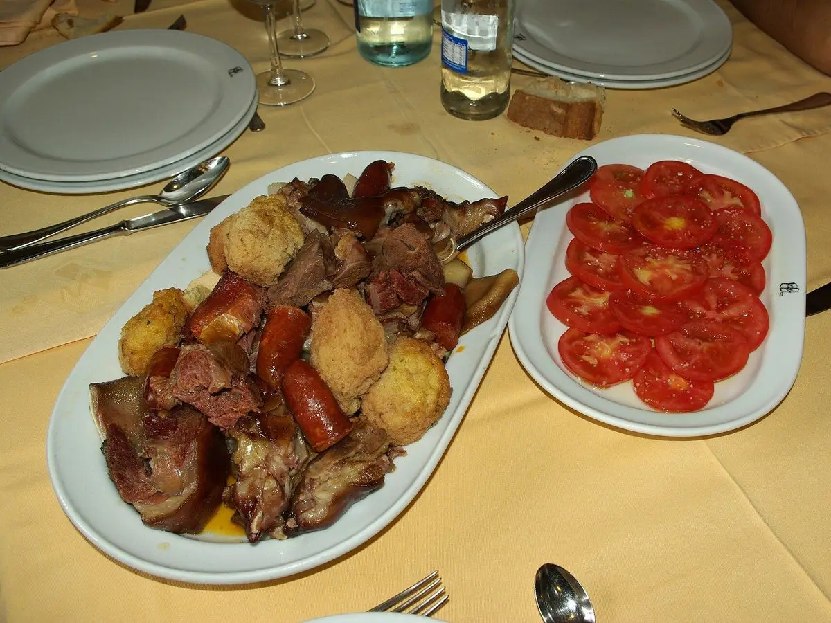 Fuente con las carnes del cocido maragato, chorizo y bolas de relleno, junto a un plato de tomate