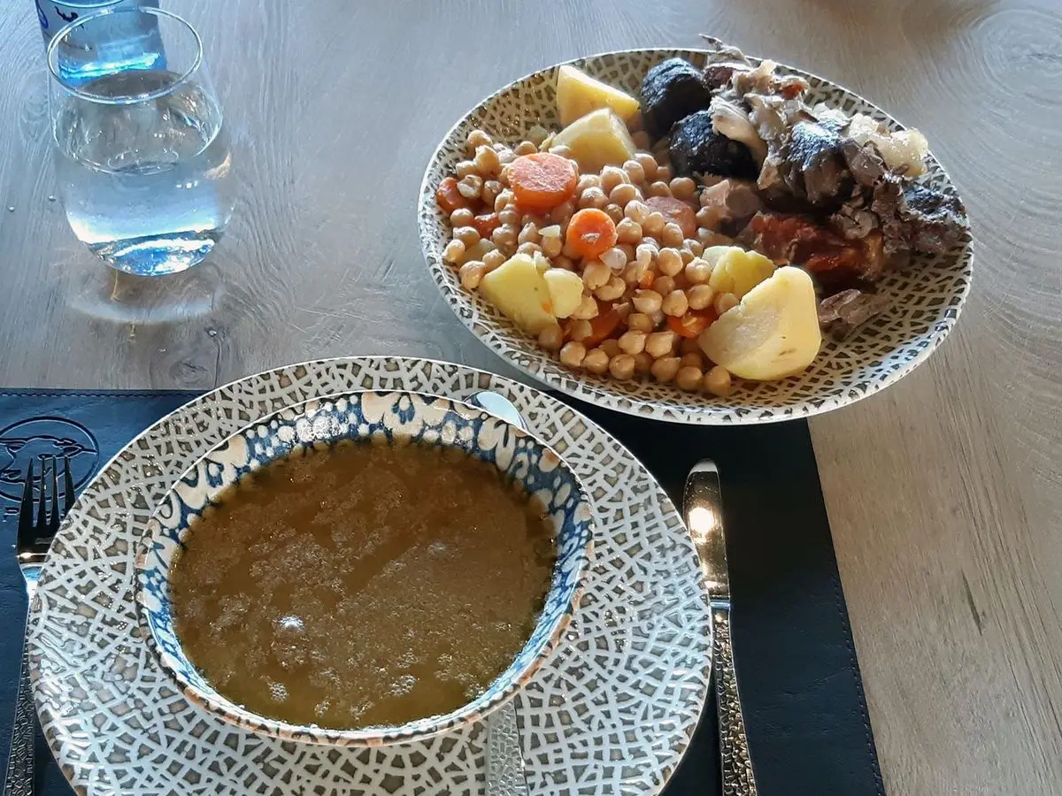 Plato de cocido con garbanzos, patata y carnes junto a un cuenco de caldo