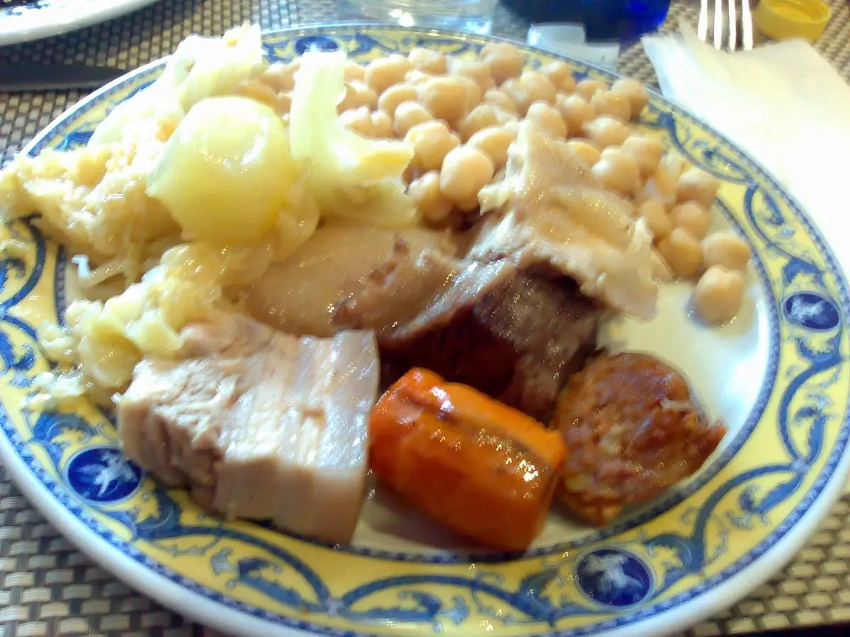 Plato de cocido con garbanzos, patata, zanahoria y carnes sobre un plato decorado azul
