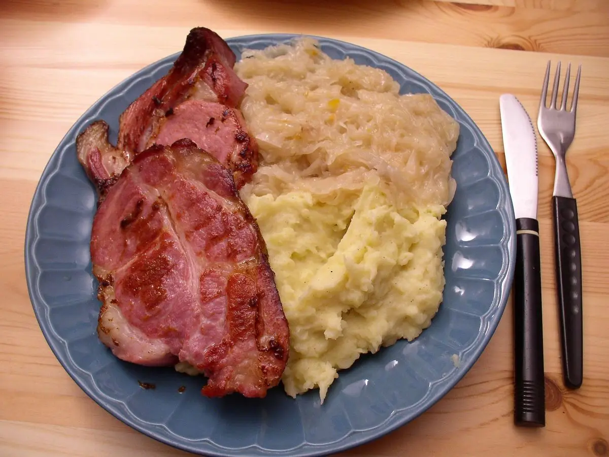 Lonchas de cerdo ahumado asado con chucrut y puré de patata en un plato azul