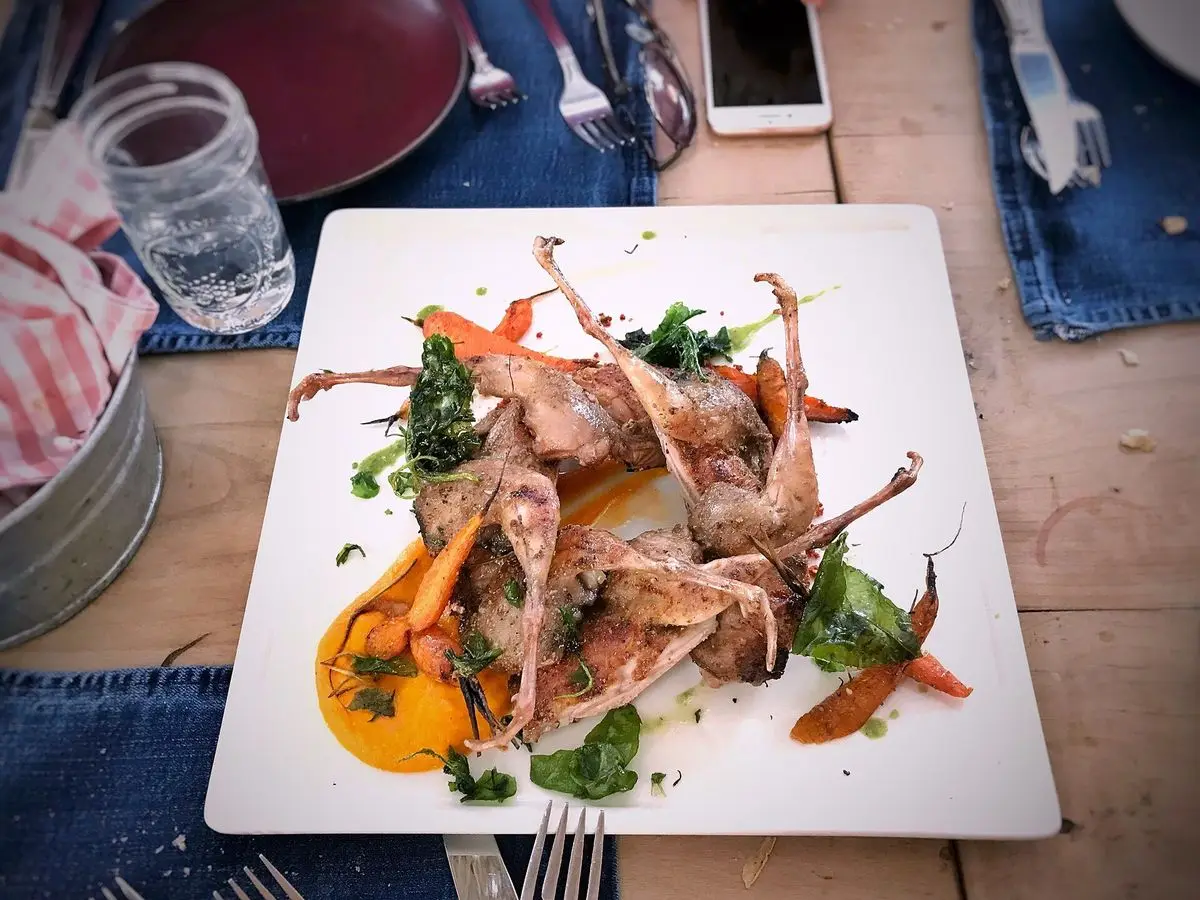 Codornices asadas con salsa anaranjada y hierbas sobre un plato cuadrado blanco