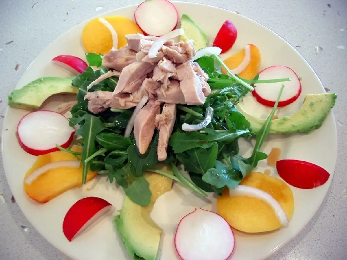 Plato de rúcula con pollo desmenuzado, aguacate, rabanitos y gajos de naranja