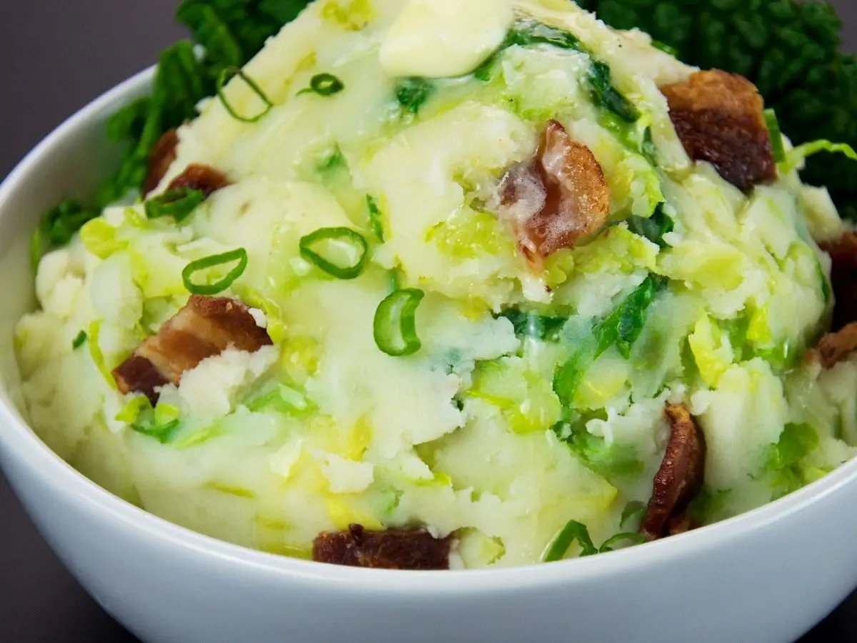 Cuenco blanco de puré de patata con col rizada, cebolleta y trocitos de bacon