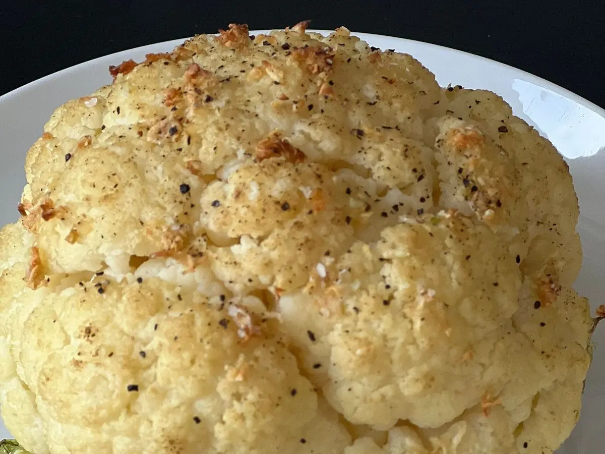 Coliflor entera asada al horno, dorada y con especias por encima, sobre un plato blanco
