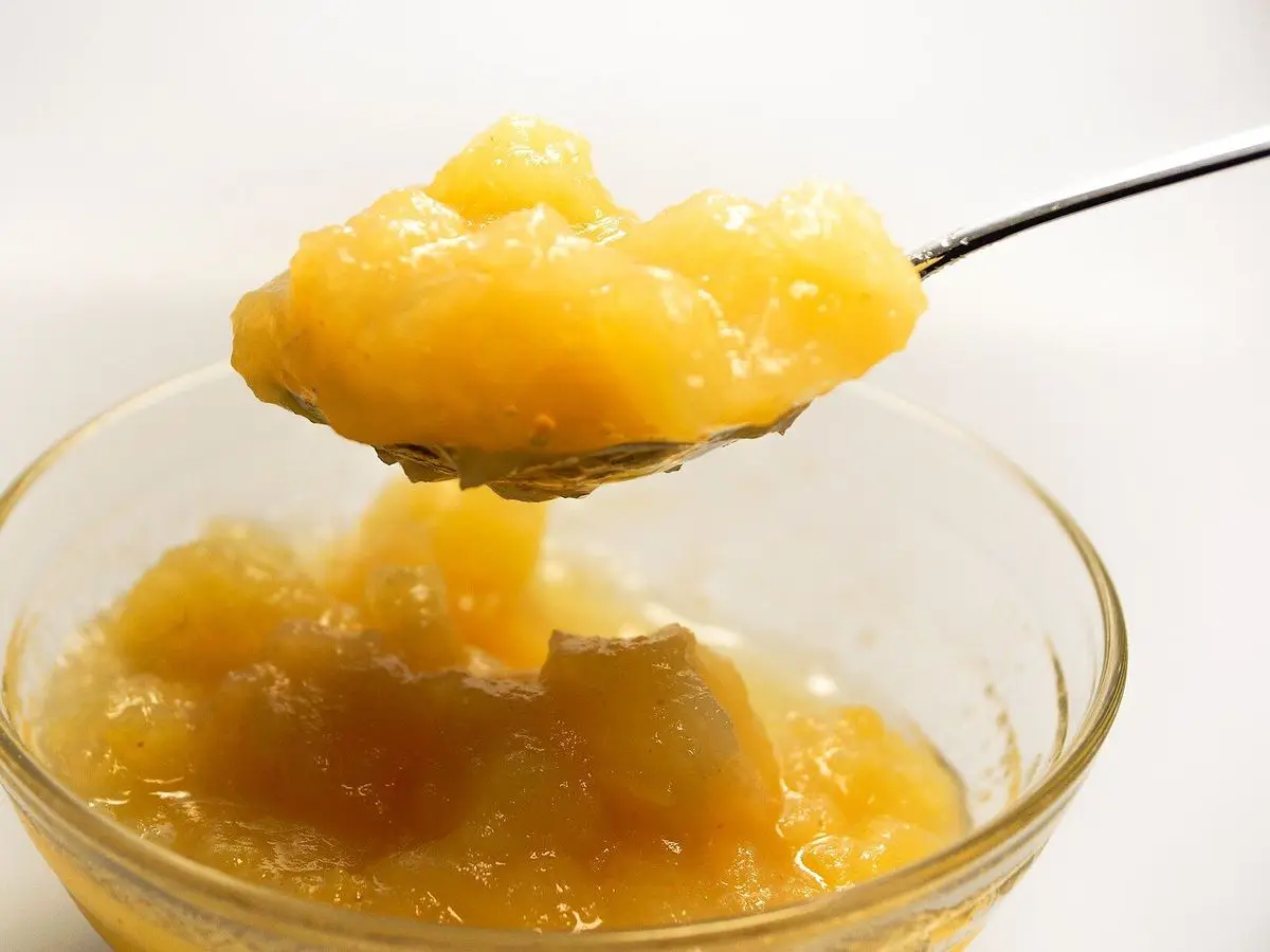 Cuchara con compota de manzana sobre un cuenco de cristal con más compota