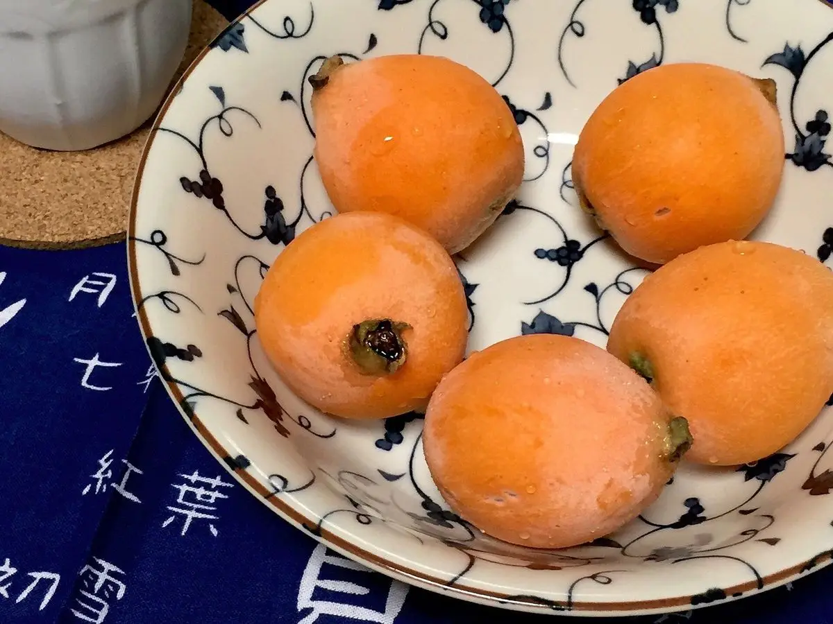 Nísperos maduros servidos en un plato de loza blanca con dibujos azules sobre un mantel azul
