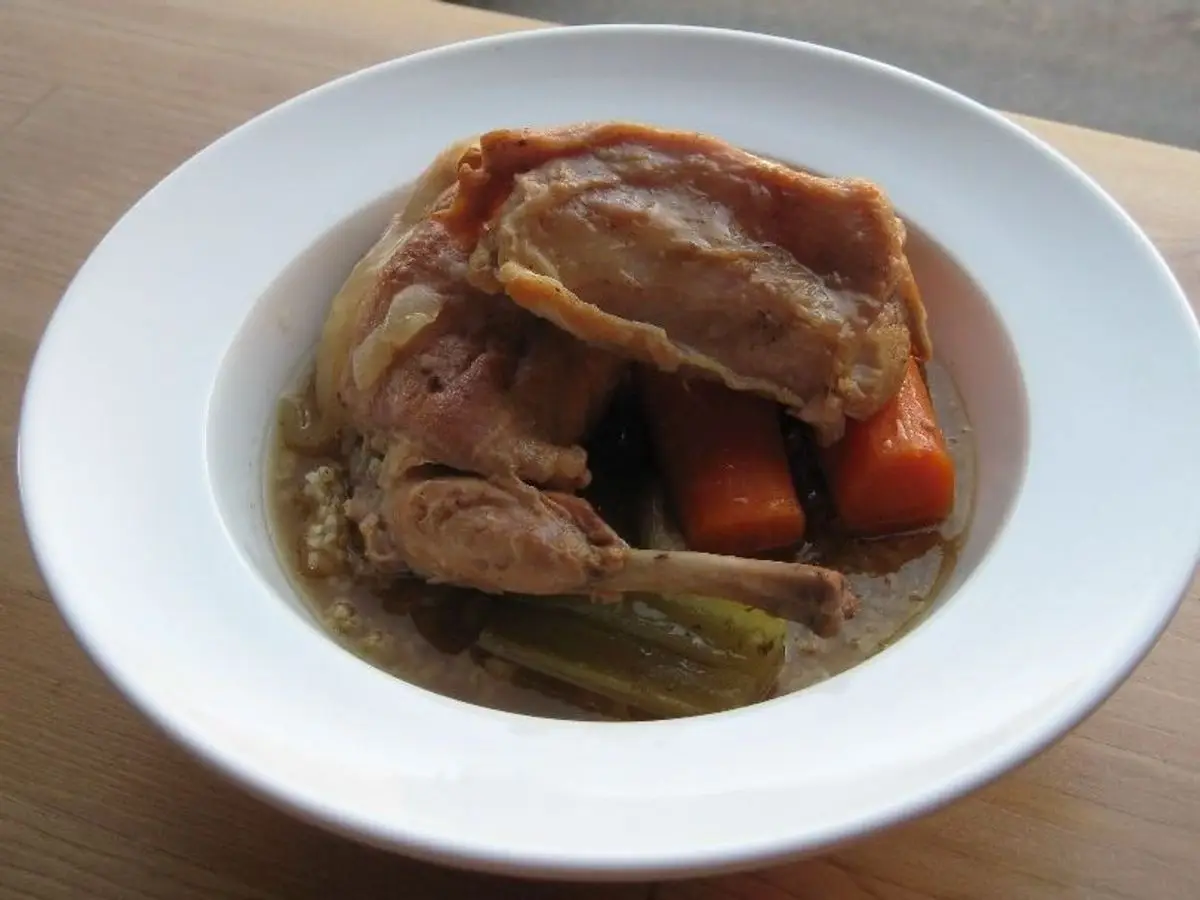 Plato hondo blanco con conejo guisado, zanahoria y hierbas en su salsa