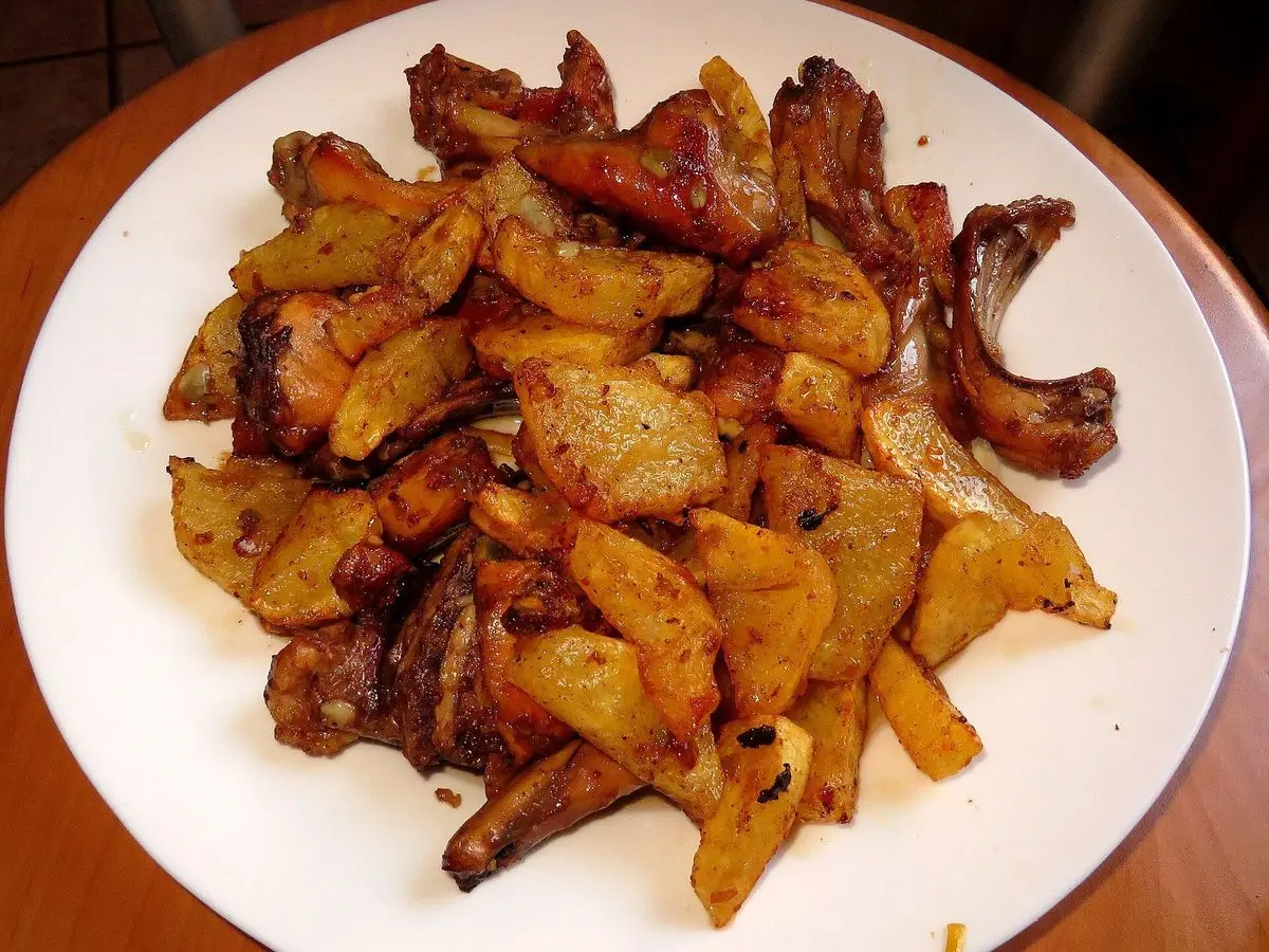 Plato de trozos de conejo dorados al ajillo con patatas fritas en gajos