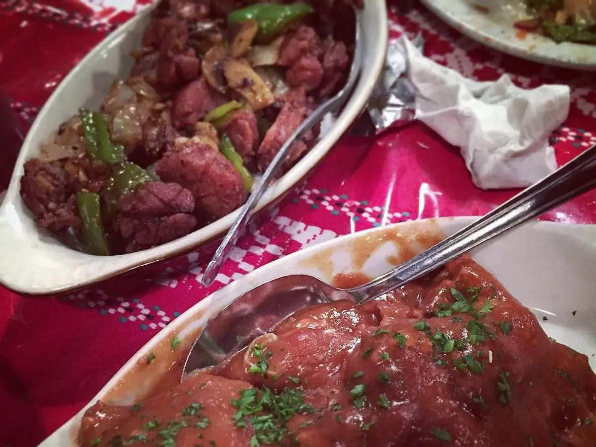 Fuente con conejo en salsa de vino tinto con hierbas picadas junto a otro plato