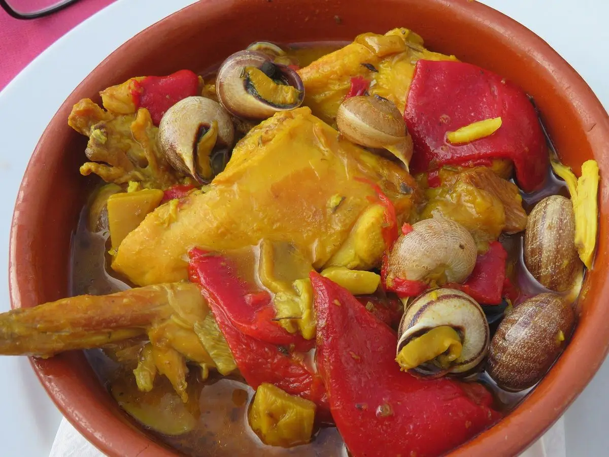 Cazuela de barro con trozos de conejo guisado, caracoles y tiras de pimiento rojo