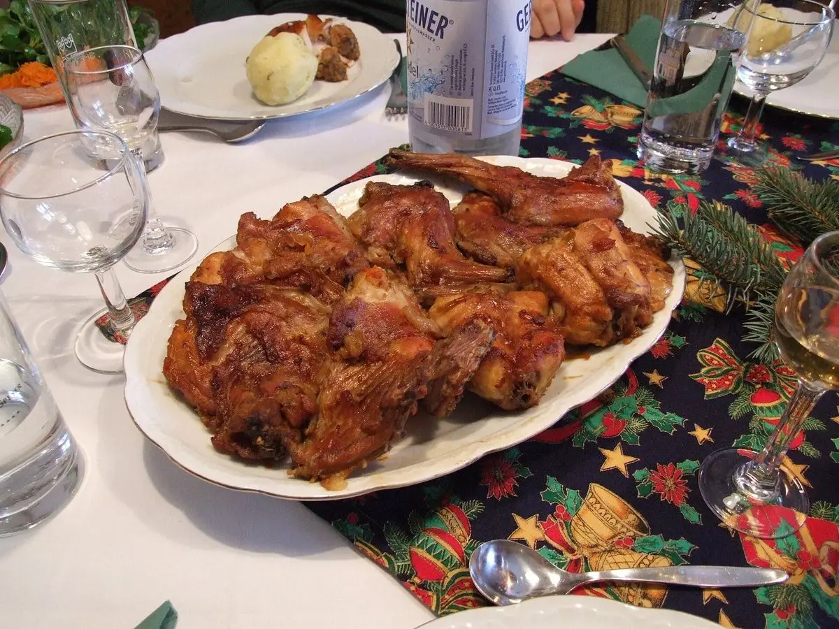 Fuente blanca con trozos de conejo asado dorado sobre mantel navideño