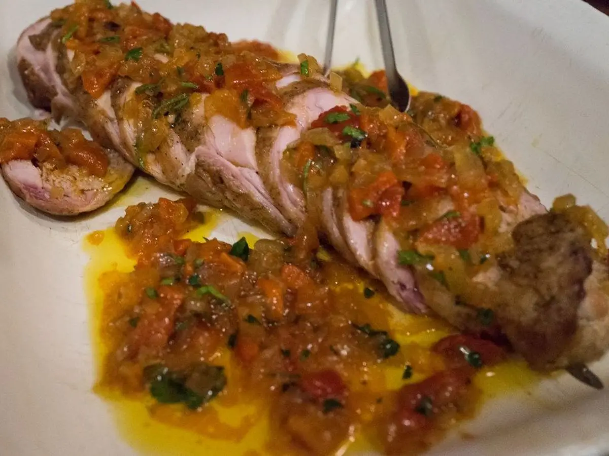 Conejo asado cortado en rodajas con salsa de tomate y pimiento y hierbas sobre un plato blanco
