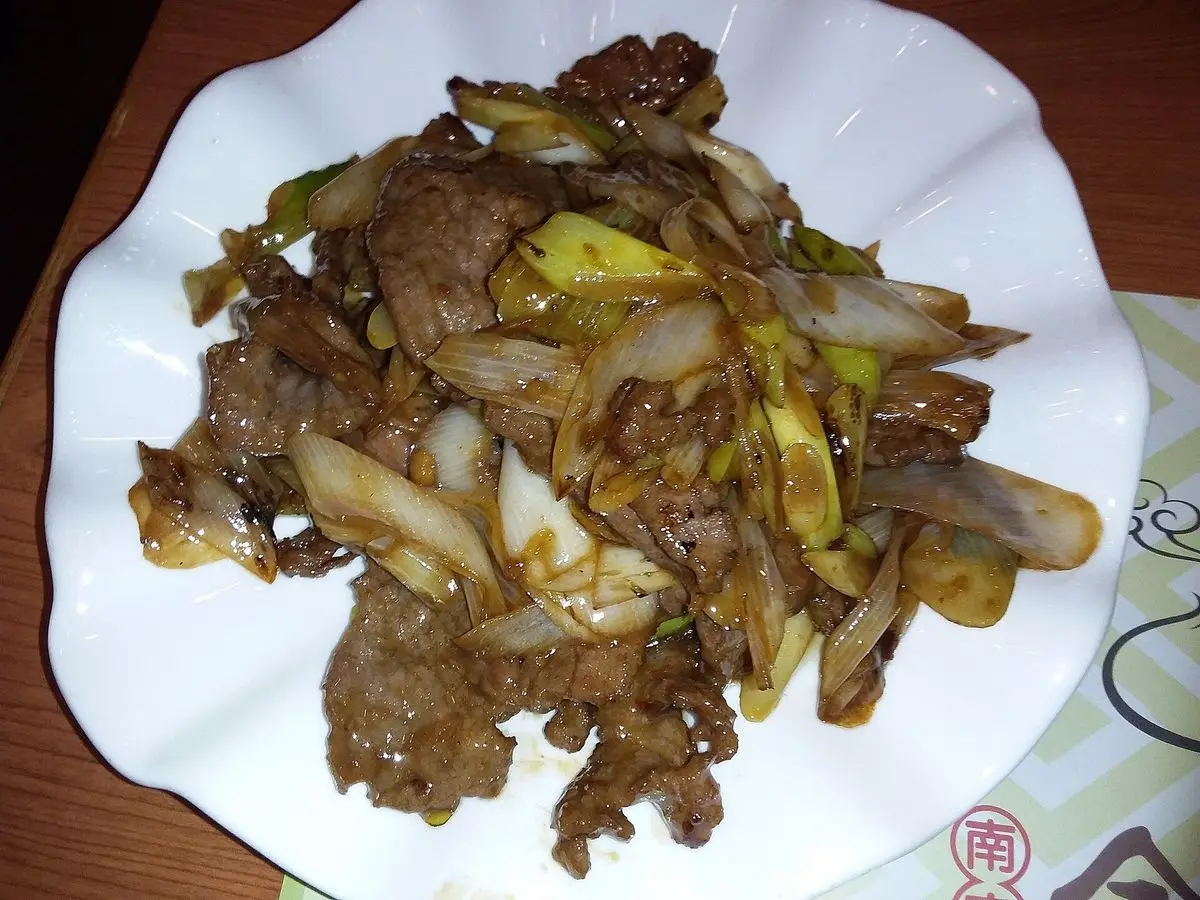 Plato blanco de ternera salteada en tiras con cebolleta y cebolla en salsa oscura
