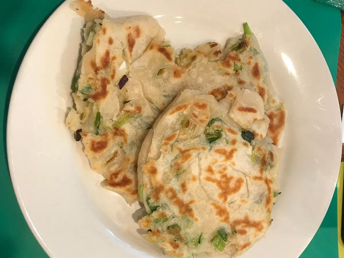 Plato blanco con tortitas chinas hojaldradas de cebolleta doradas y cortadas