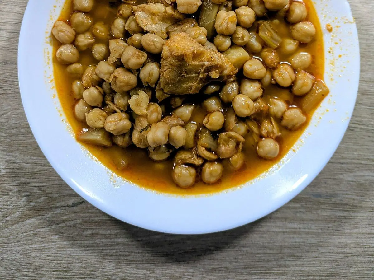 Plato hondo de garbanzos guisados con trozos de pescado y patata en caldo de tomate