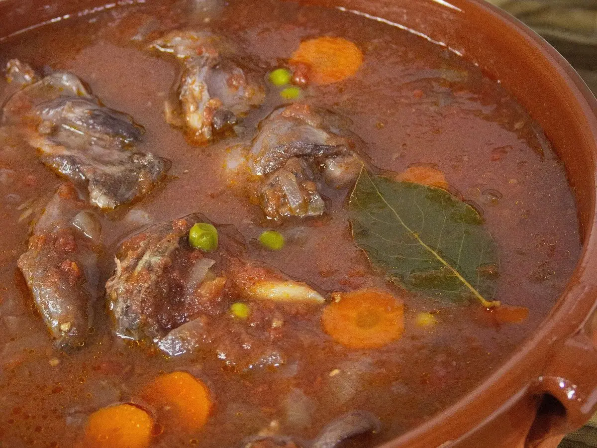 Cazuela de barro con conejo guisado en salsa, zanahoria, guisantes y hojas de laurel
