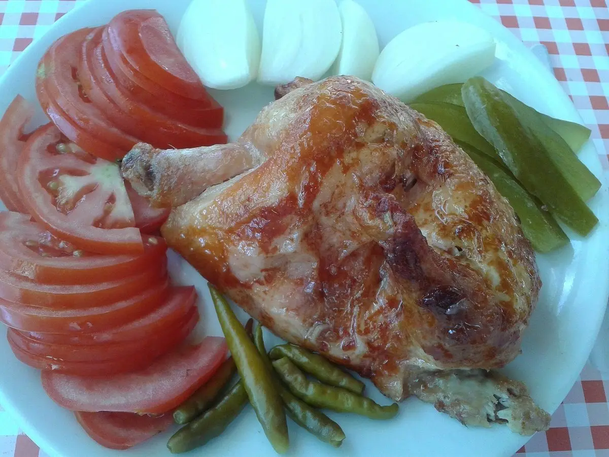 Muslo de pollo asado con rodajas de tomate, cebolla y judías verdes en un plato sobre mantel de cuadros