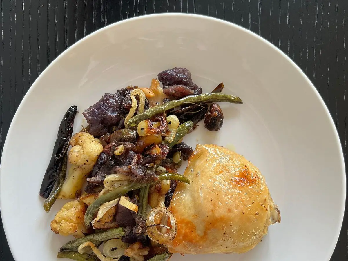 Plato blanco con muslo de pollo dorado y verduras asadas: berenjena, judías verdes y champiñones