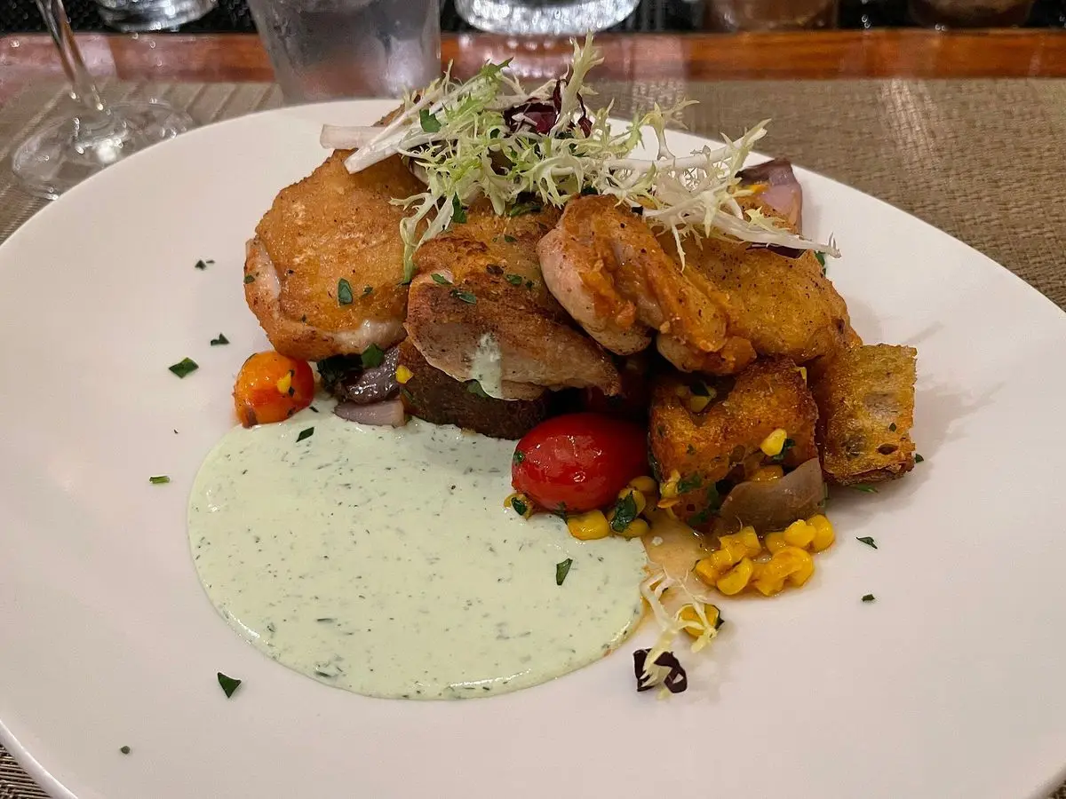 Plato blanco con muslos de pollo asados, tomate cherry, chalota asada y salsa de hierbas