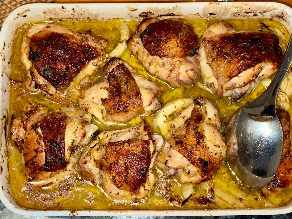 Bandeja de horno con contramuslos de pollo dorados braseados con hinojo y naranja y una cuchara
