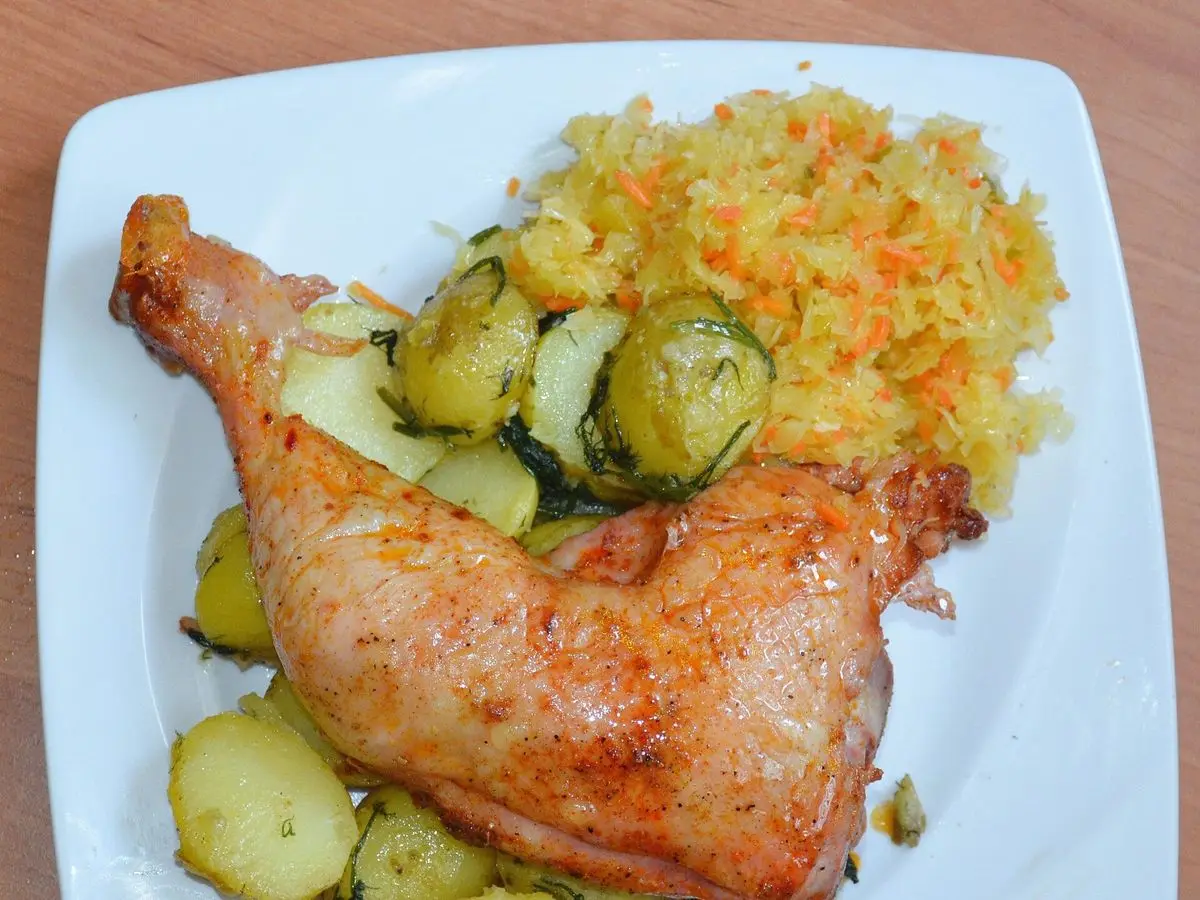 Muslo de pollo asado con patatas hervidas y ensalada de zanahoria rallada en un plato blanco