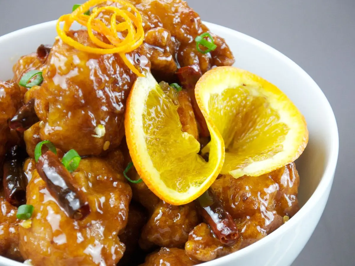 Cuenco blanco con pollo glaseado en salsa de naranja y rodajas de naranja