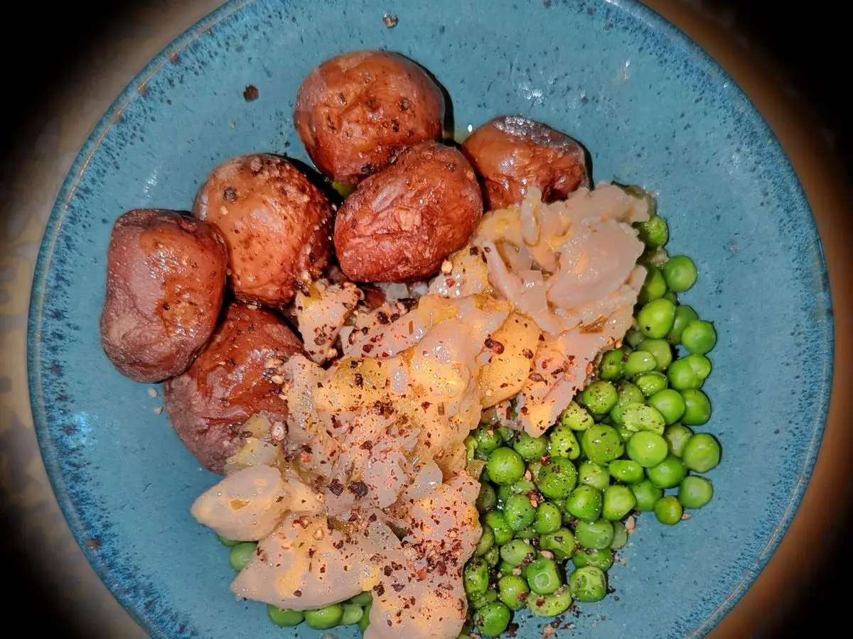 Plato azul con pollo en salsa, patatas pequeñas cocidas y guisantes verdes