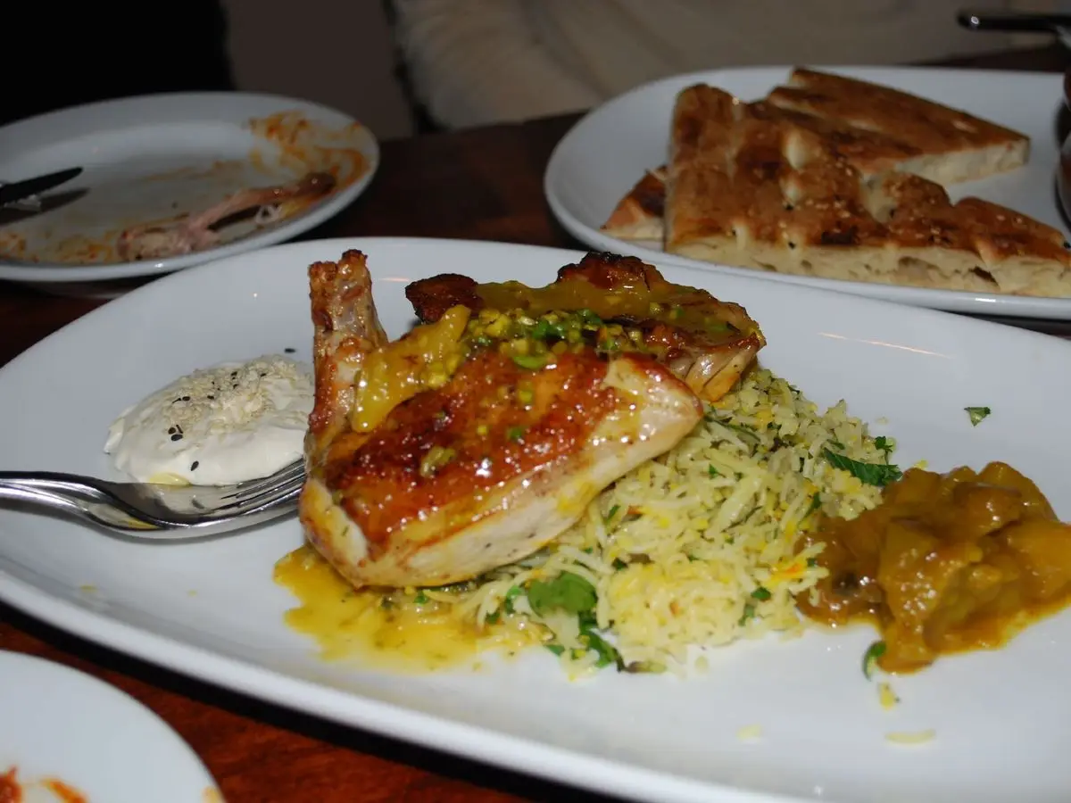 Plato blanco con pollo asado dorado sobre arroz pilaf con salsa de yogur y chutney a un lado