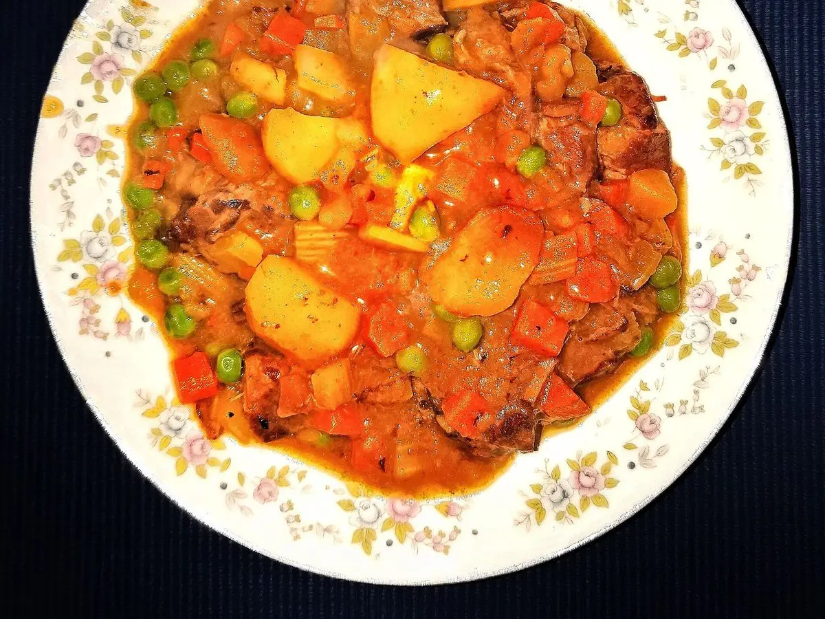 Guiso de carne con patatas, guisantes y tomate en un plato decorado con flores