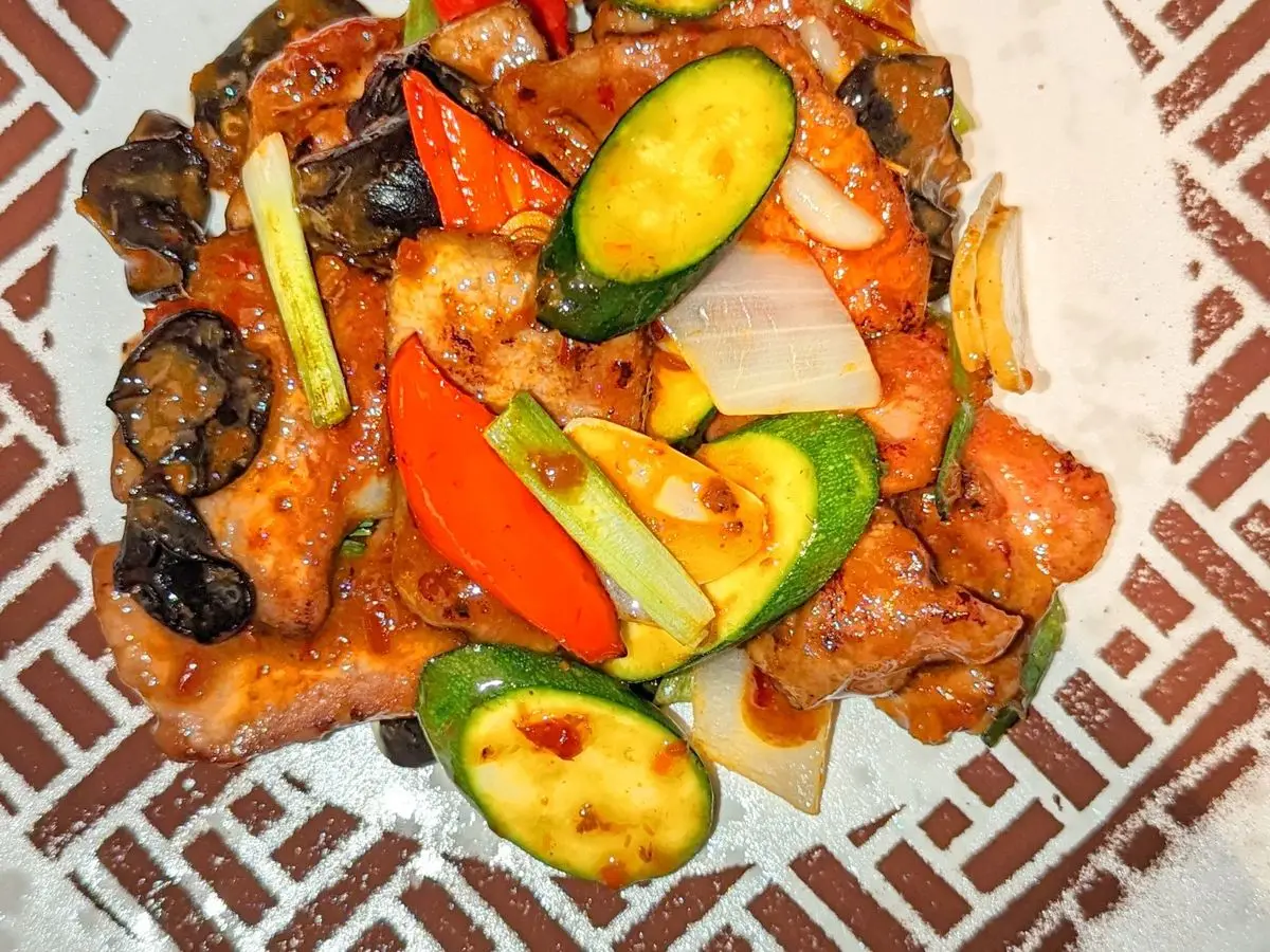 Cordero salteado con pimiento rojo, calabacín, cebolla y setas negras en un plato blanco