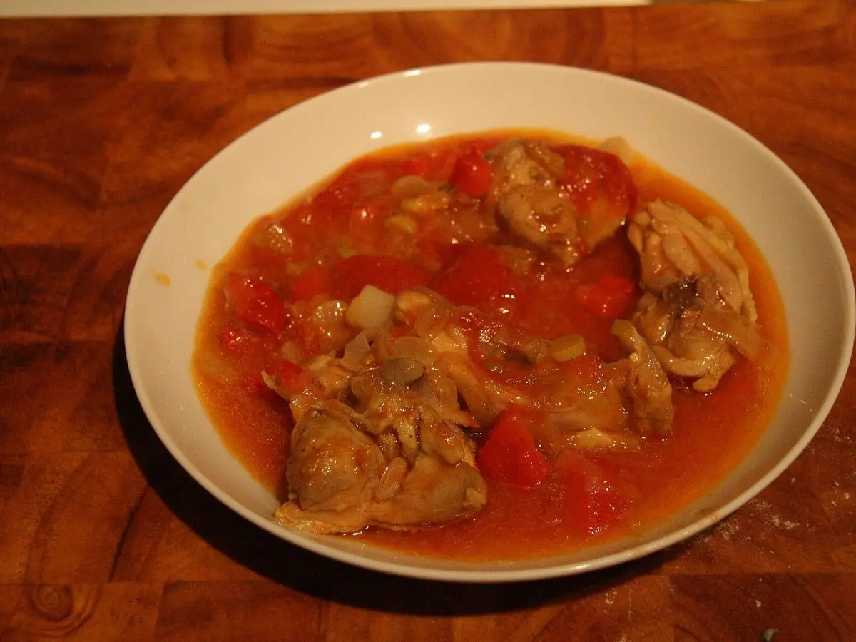 Plato hondo de trozos de carne guisados en salsa roja de pimiento y tomate sobre mesa de madera