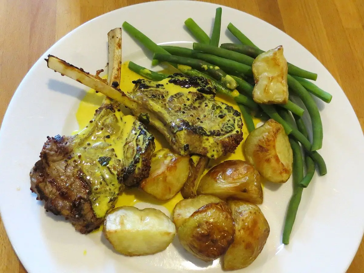 Plato blanco con chuletillas de cordero a la hierba, patatas asadas pequeñas y judías verdes