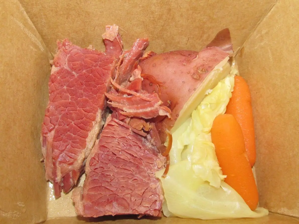 Corned beef en lonchas con col cocida y zanahoria en una caja de cartón