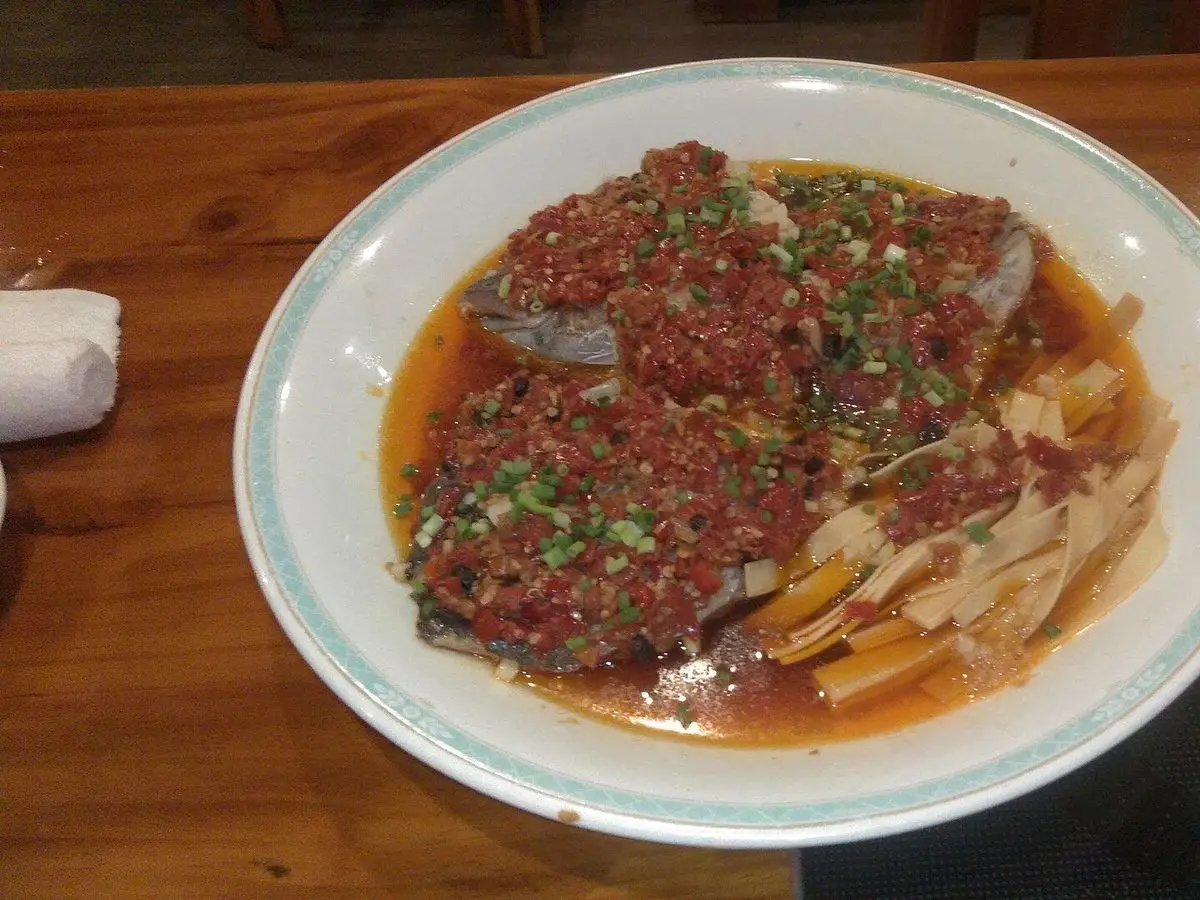 Pescado al vapor cubierto de guindilla roja picada en salsa, servido en un plato blanco