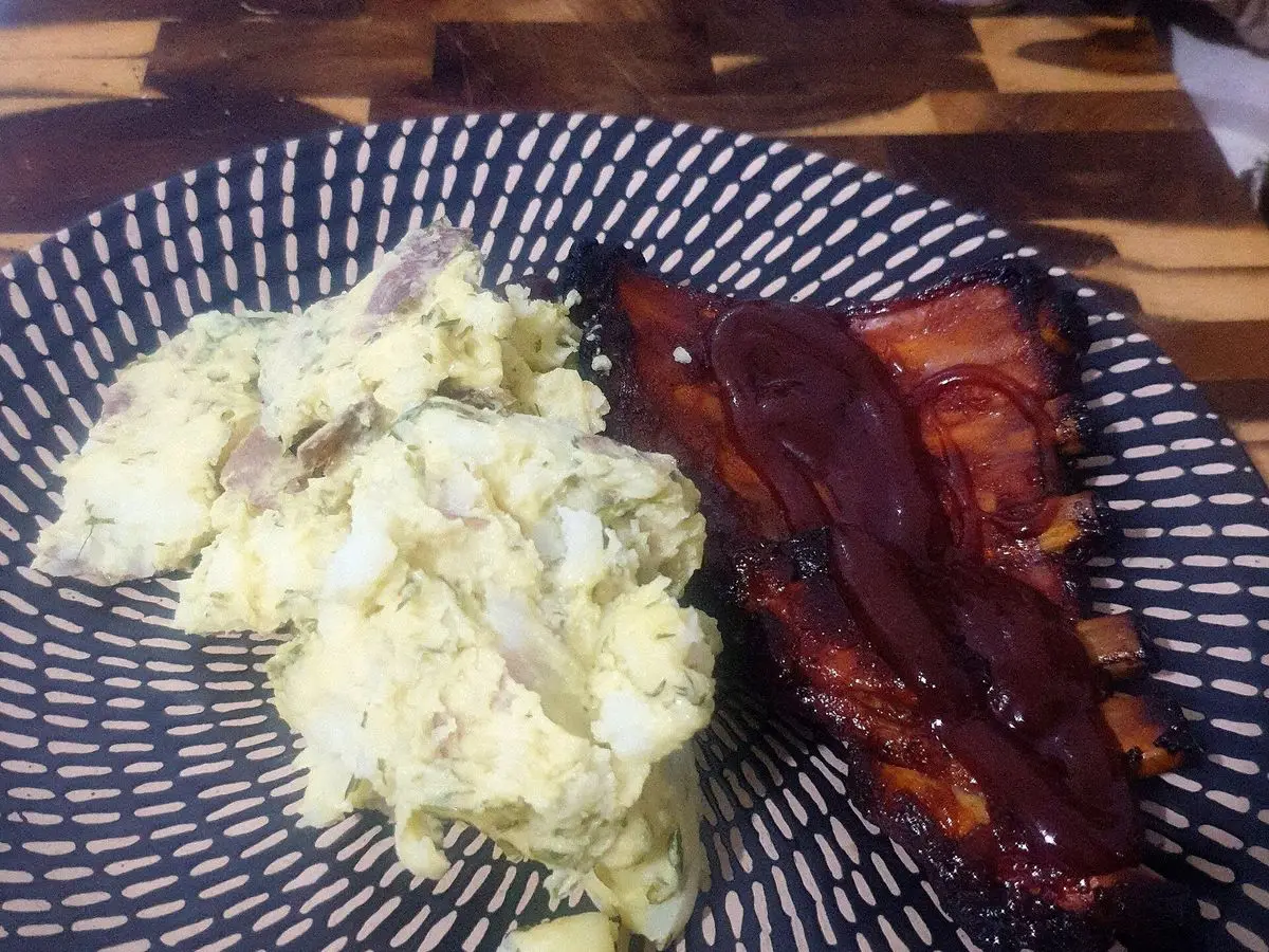 Costillas de cerdo glaseadas con salsa barbacoa junto a ensalada de patata en un plato negro