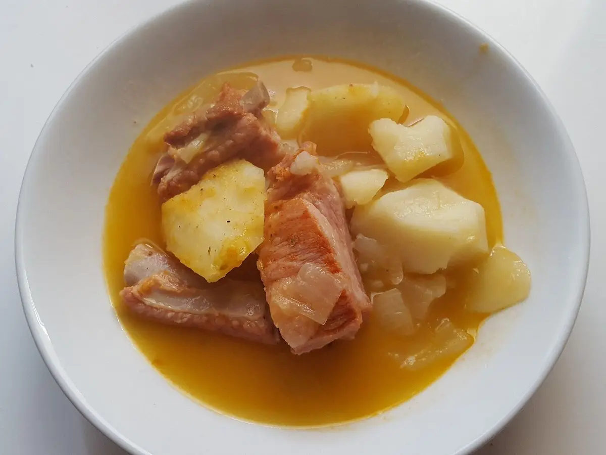 Plato blanco con trozos de cerdo, patata y caldo amarillo