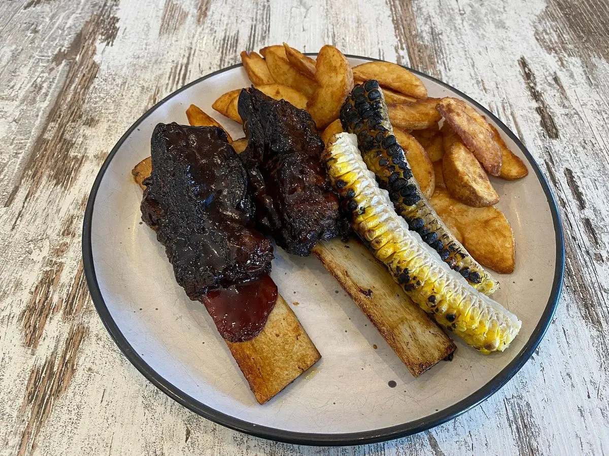 Costillas de ternera glaseadas con salsa barbacoa, mazorca de maíz asada y patatas gajo en un plato