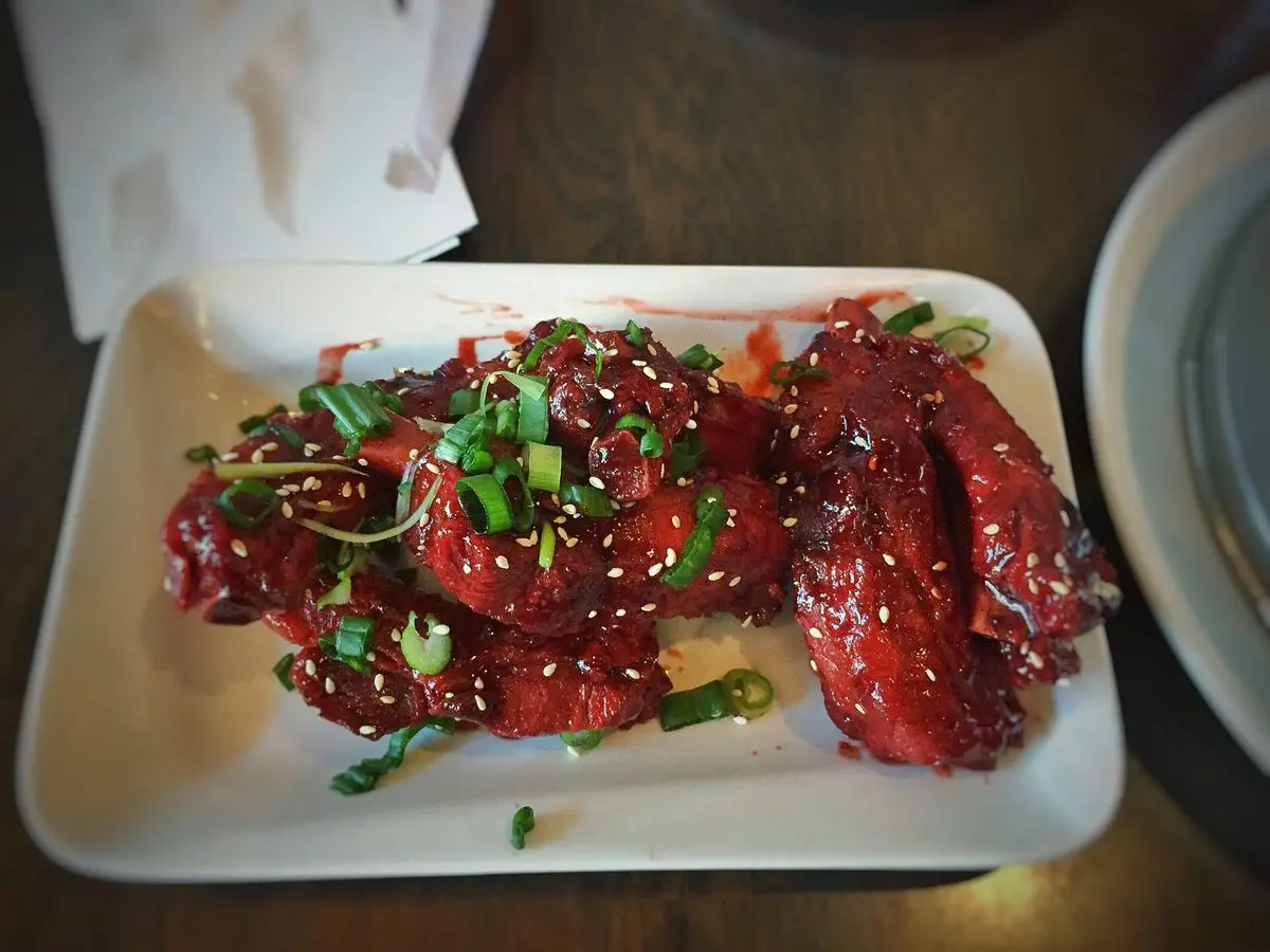 Costillas de cerdo lacadas con sésamo y cebolleta picada sobre un plato rectangular blanco