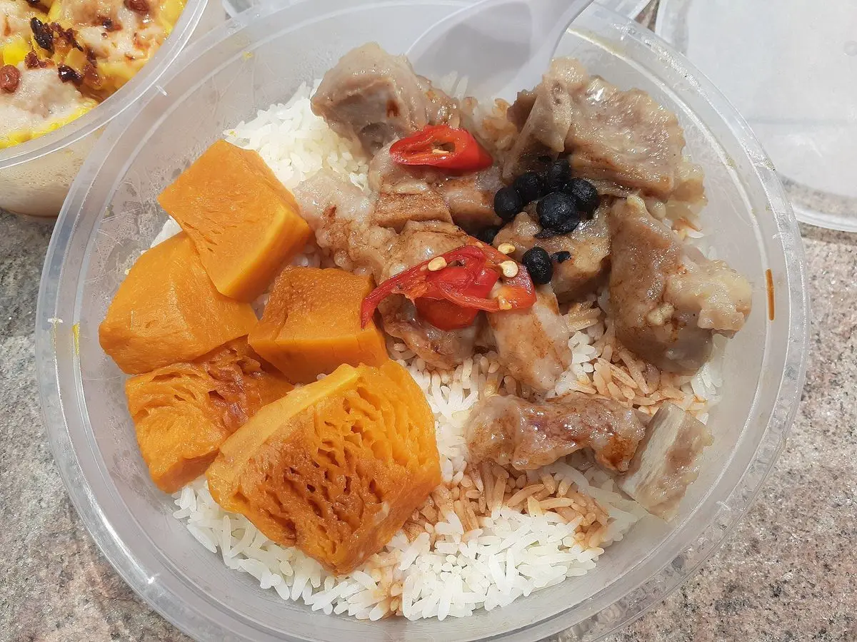 Costillitas de cerdo al vapor con guindilla roja y calabaza sobre arroz blanco en un recipiente