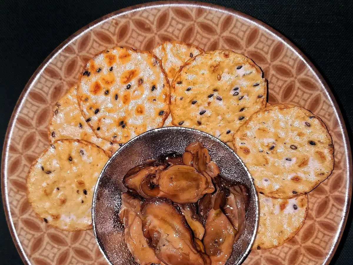 Galletas saladas redondas con semillas de sésamo sobre un plato con un cuenco pequeño en el centro