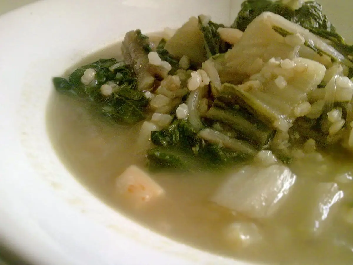 Plato hondo de sopa clara de acelgas con patata y arroz sobre plato blanco