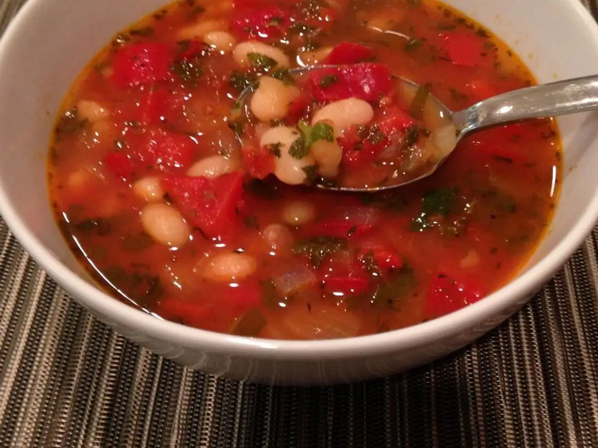 Cuenco de sopa de alubias blancas con tomate y pimiento rojo, con cuchara