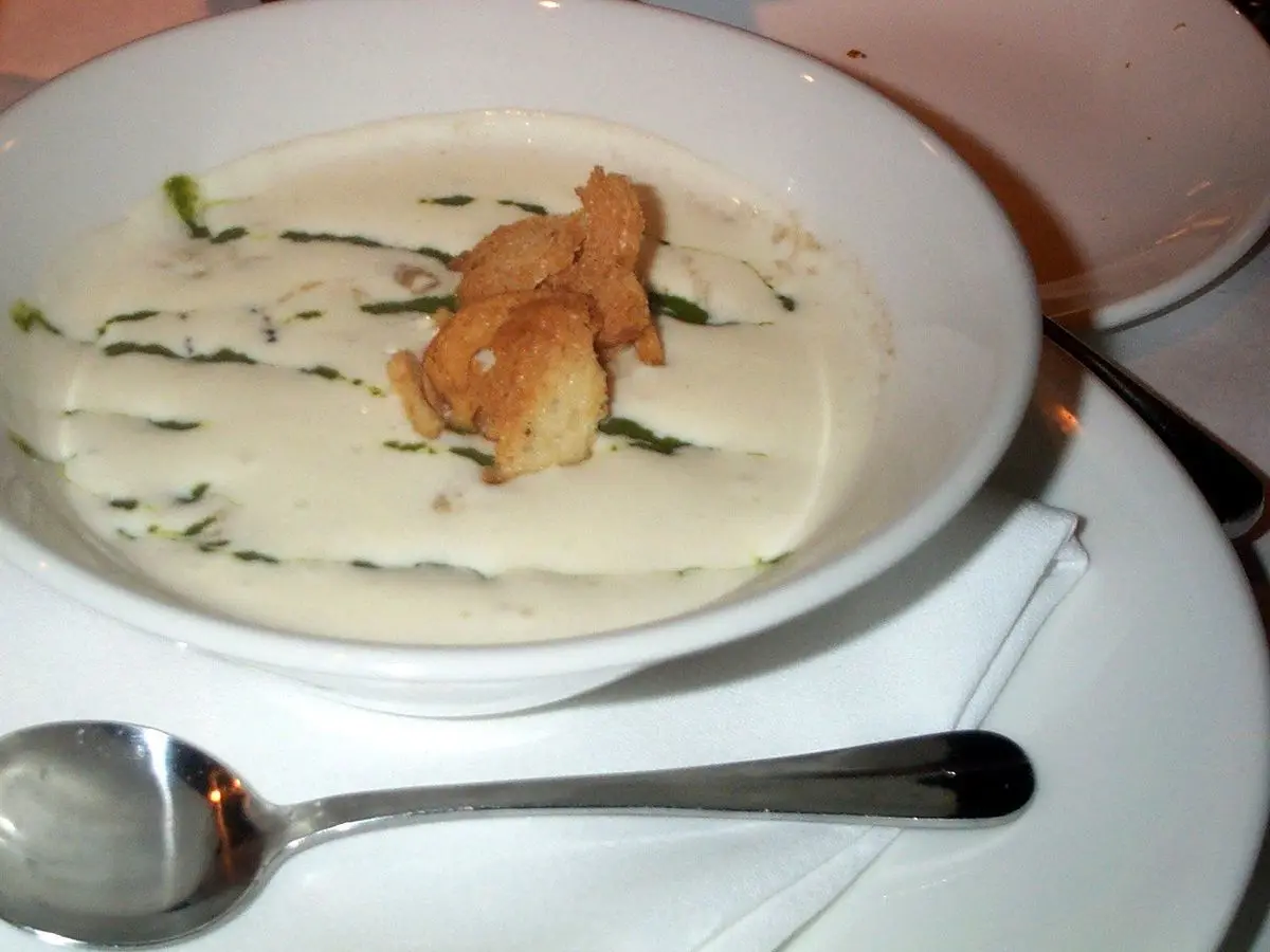 Plato hondo de crema blanca de verduras con picatostes y hierbas, con cuchara