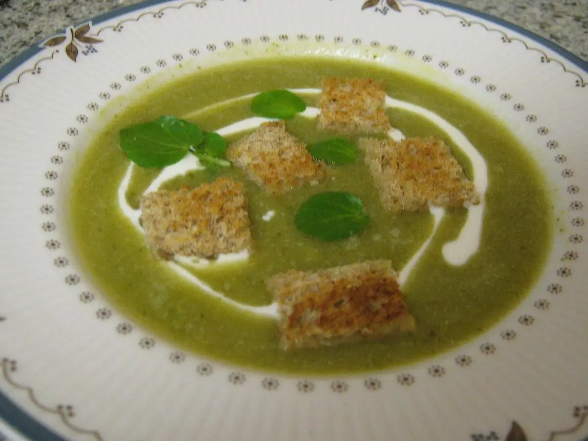 Plato hondo de crema verde de berros con hojas pequeñas, un hilo de nata y dados de pan tostado