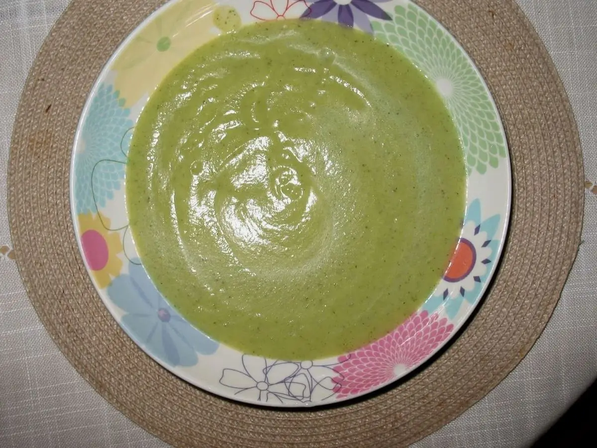 Plato hondo de crema verde de calabacín lisa y espesa con un borde de flores de colores