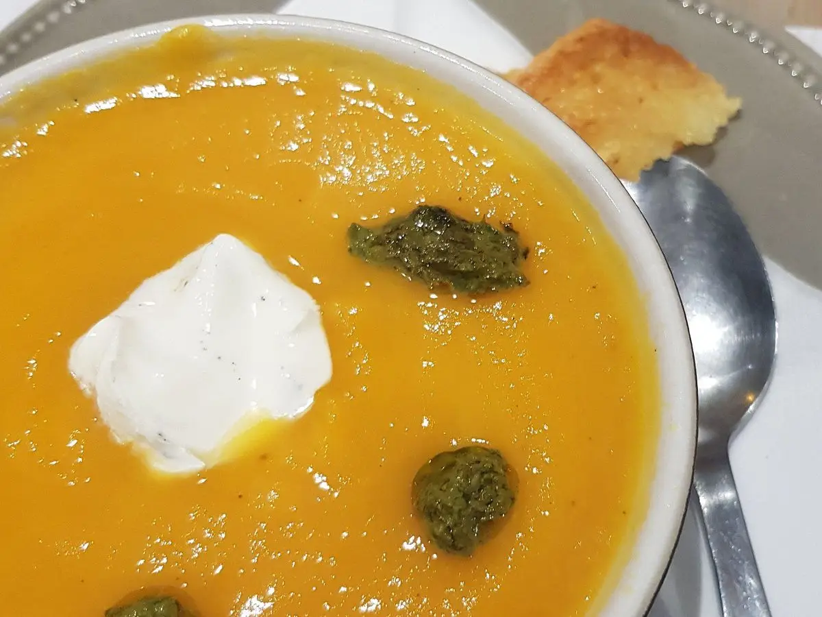 Plato hondo de crema de calabaza naranja con una cucharada de queso cremoso y trocitos verdes