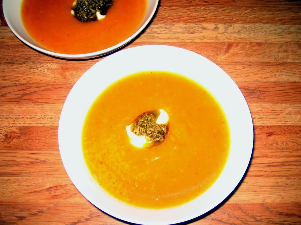 Plato blanco de crema anaranjada de calabaza con un toque de hierbas sobre una mesa de madera