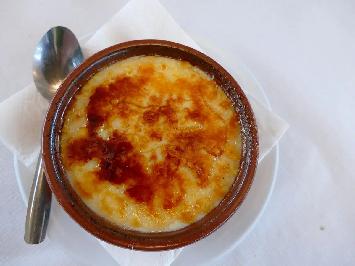 Cazuela de barro con crema catalana y su capa de azúcar caramelizado, con una cuchara al lado