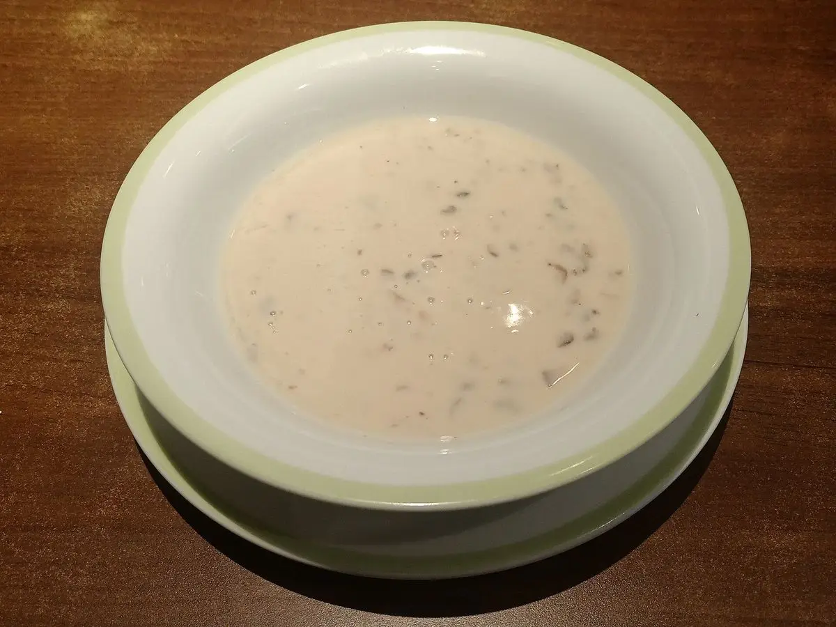 Plato hondo de crema blanca de champiñones con hierbas picadas sobre una mesa de madera